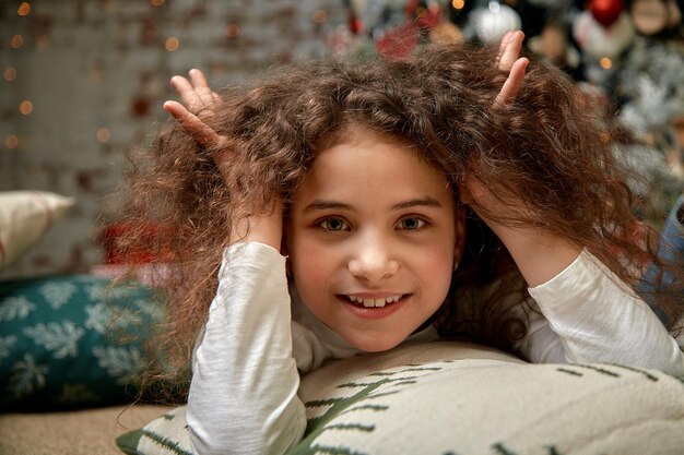 Uma linda garota com cabelo encaracolado escuro fica na sala de estar perto da lareira conceito de ano novo Emoções engraçadas no dia de inverno