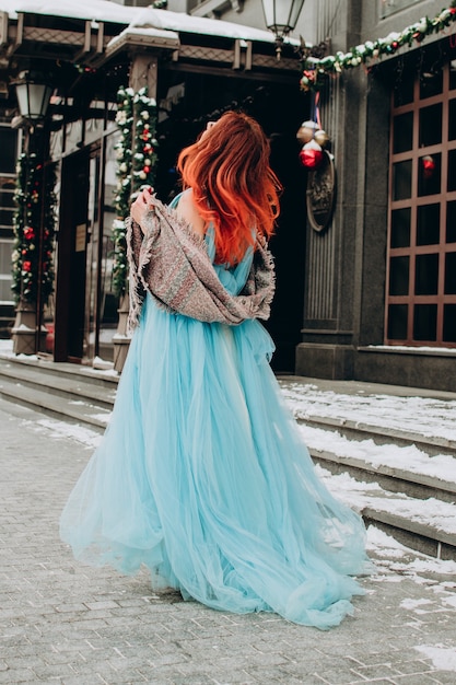 Uma linda garota com cabelo vermelho em um longo vestido azul está de costas