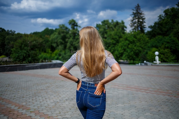 Foto uma linda garota com longos cabelos loiros de aparência europeia. vestido com jeans e uma camiseta. caminhe em um dia ensolarado