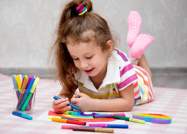 Uma linda garota com roupas de arco-íris desenha um arco-íris com marcadores multicoloridos