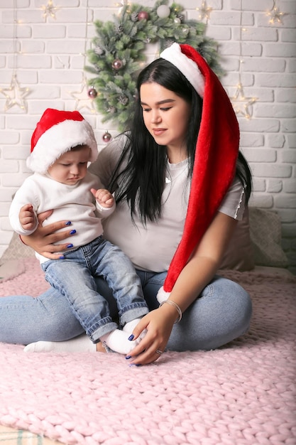 uma linda garota com um chapéu de Papai Noel está sentada na cama abraçando seu filho