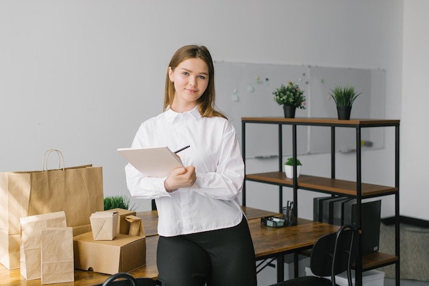 Uma linda garota com um notebook e olha para os pacotes ecológicos em pé na mesa do escritório