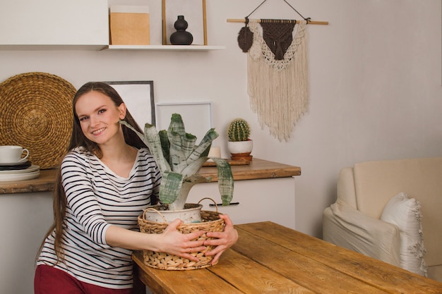 Uma linda garota com um suéter listrado está em uma cozinha escandinava e abraça uma flor dentro de casa