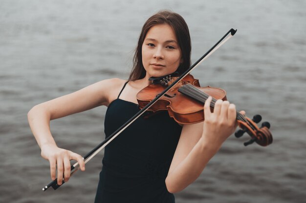 Uma linda garota com um violino fica no contexto da água. Aparência asiática. conceito musical. Foto de alta qualidade