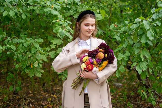 Uma linda garota com uma faixa preta e cabelos longos segura um buquê de flores de outono e corrige-o