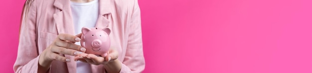 Uma linda garota com uma jaqueta rosa está segurando um cofrinho 3d em suas mãos Belo retrato em estúdio em rosa
