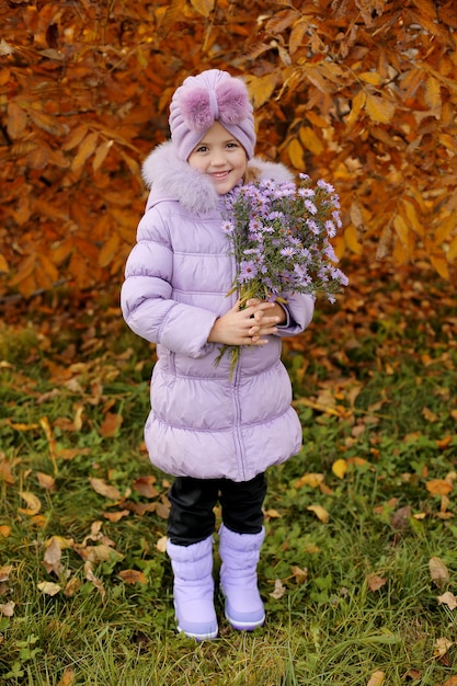 Uma linda garota com uma jaqueta roxa bota turbante com flores de outono nas mãos