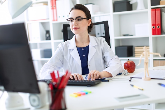 Uma linda garota com uma túnica branca está sentada à mesa e digitando no teclado.