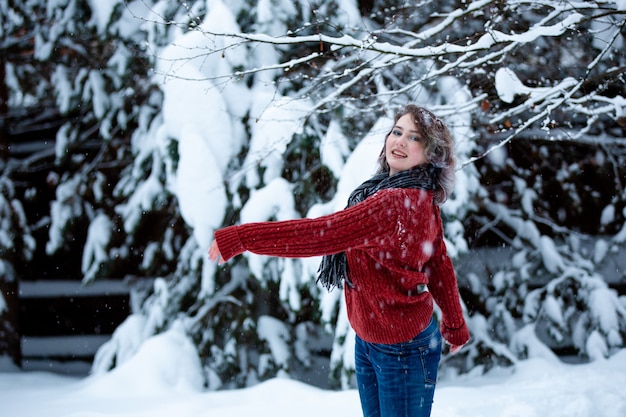 Uma linda garota de aparência caucasiana com um suéter bordô lança neve.