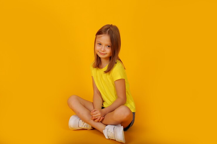 Foto uma linda garota de cabelos castanhos em uma camiseta amarela e shorts está sentada sobre um fundo amarelo