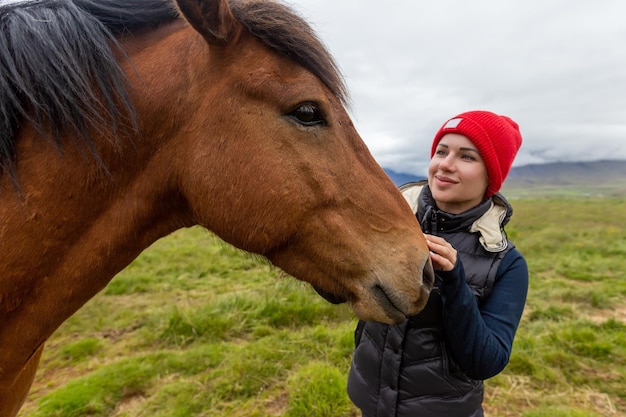 Uma linda garota de chapéu vermelho está olhando para um cavalo islandês. Islândia