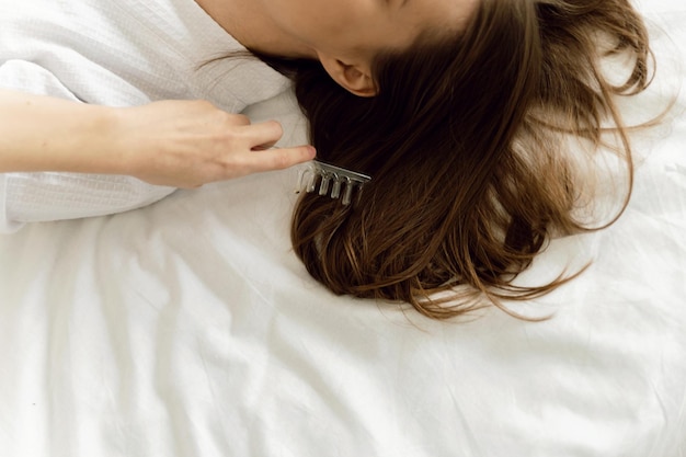 uma linda garota de jaleco branco sorrindo penteia o cabelo com um pente ecológico. conceito de cuidado de cabelo.