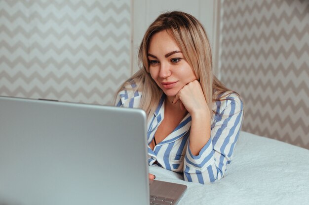 Foto uma linda garota de pijama está deitada na cama atrás de um laptop