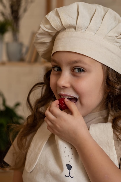 uma linda garota de seis anos com um chapéu de chef come framboesas