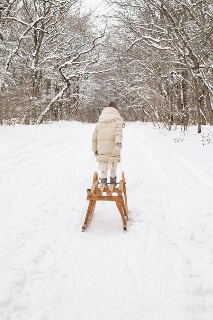uma linda garota de seis anos rola um trenó de madeira em uma estrada de neve no parque