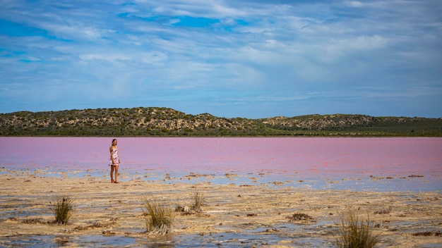 Uma linda garota de vestido branco caminha ao longo da margem de um lago rosa na austrália ocidental