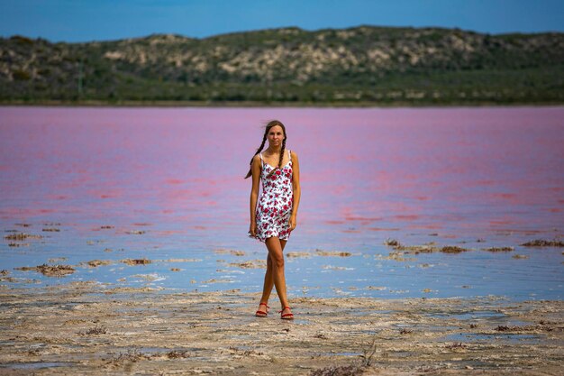 Uma linda garota de vestido branco caminha ao longo da margem de um lago rosa na austrália ocidental