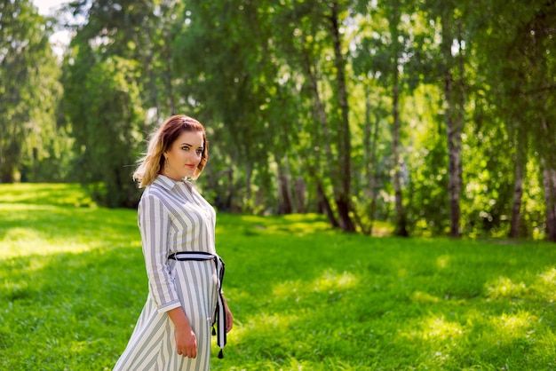 Uma linda garota de vestido branco caminha no parque em um dia de verão.