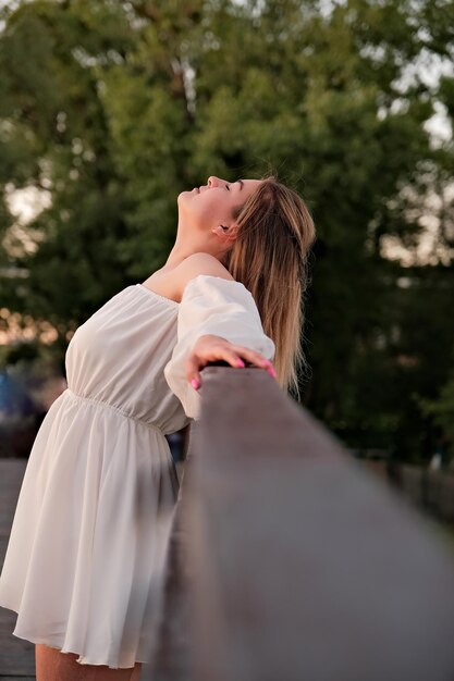 Uma linda garota de vestido branco fica em uma ponte de madeira