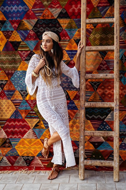 Uma linda garota de vestido branco fica perto de um tapete marroquino. Essaouira. Marrocos
