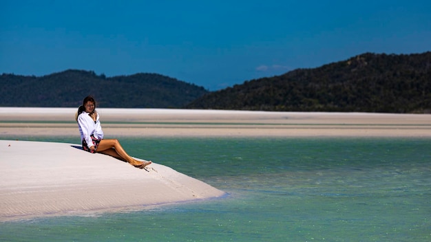 uma linda garota de vestido, camisa e chapéu senta-se nas dunas na praia de whitehaven