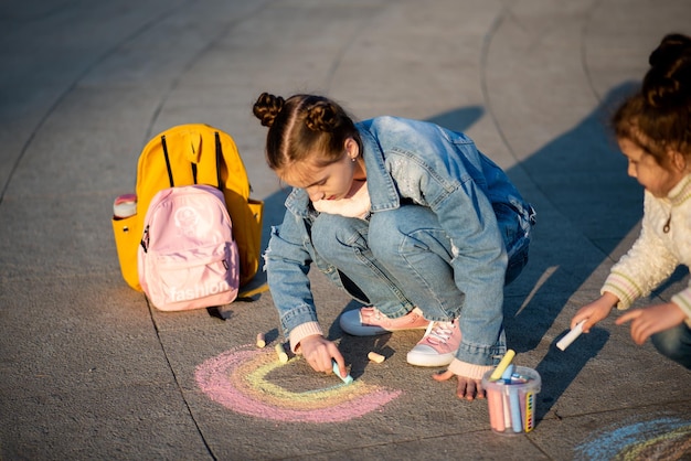 Uma linda garota desenha um arco-íris com giz de cera na rua Creation Kids Street