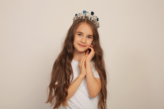 uma linda garota doce e feliz com cabelo comprido em uma camiseta branca com uma coroa na cabeça