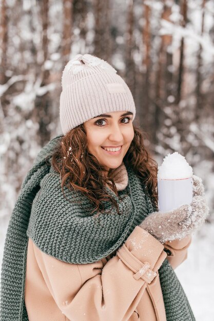 Uma linda garota em um cachecol e luvas segura uma caneca com neve