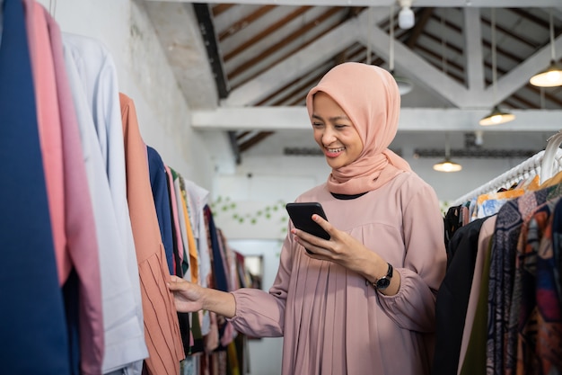 Uma linda garota em um hijab escolhendo roupas enquanto segura um smartphone