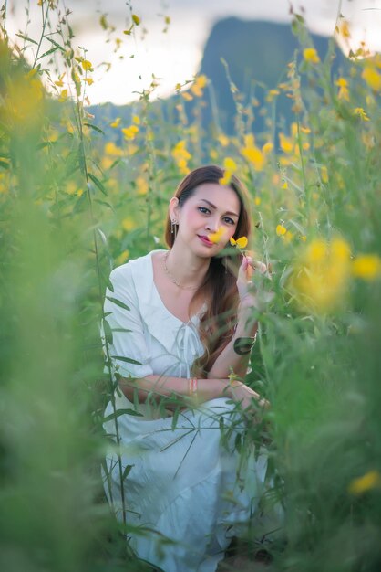 Uma linda garota em um vestido branco fotografada no meio de um campo amarelo com flores ao pôr do sol.