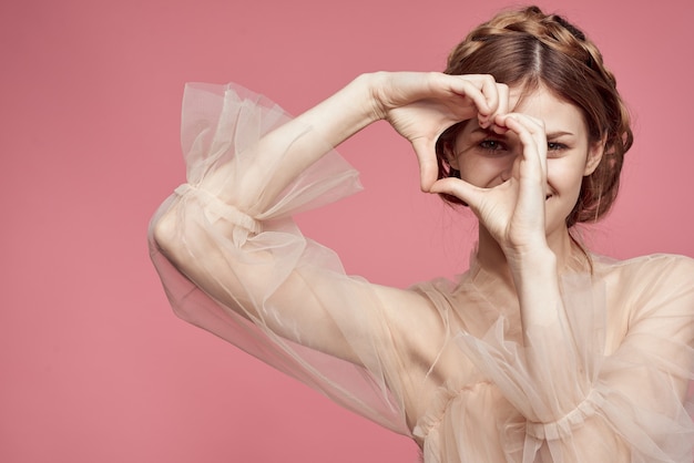 Uma linda garota em um vestido delicado mostra com as mãos um sinal de coração e amor e sorri