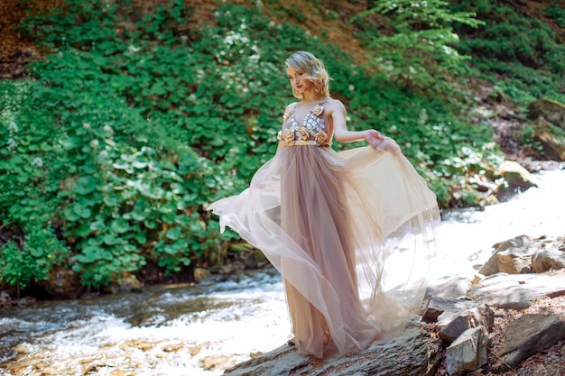 Uma linda garota em um vestido fica perto do leito do rio ao ar livre