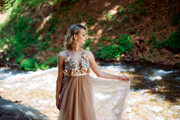 Uma linda garota em um vestido fica perto do leito do rio ao ar livre