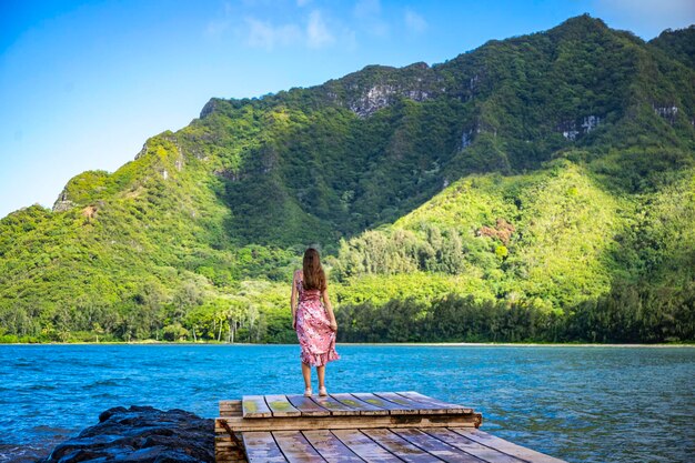 Foto uma linda garota em um vestido longo fica em um píer sobre o oceano em uma baía cercada por montanhas