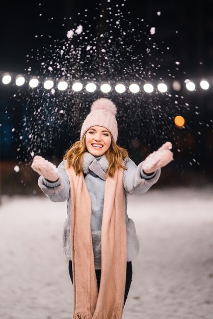 Uma linda garota está brincando com a neve. Feliz inverno na floresta. Luzes festivas