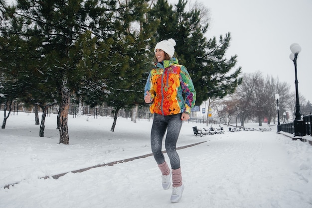 Uma linda garota está correndo em um dia gelado e com neve. Esportes, estilo de vida saudável.