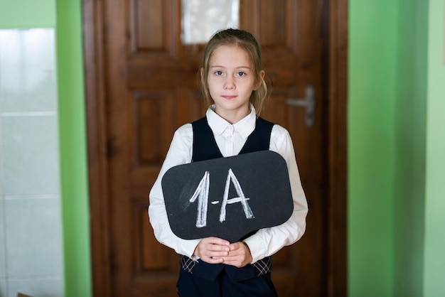 Uma linda garota está de pé na sala de aula com um sinal de 1º ano vida escolar