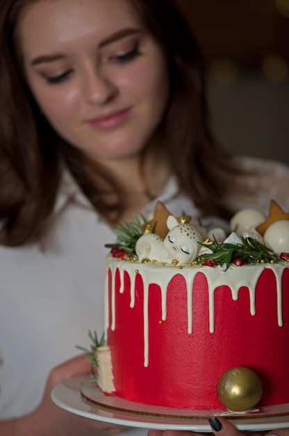 Uma linda garota feliz em uma camiseta branca fica em casa segura um bolo festivo de Ano Novo em um prato