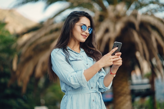 Uma linda garota jovem em um vestido azul de pé em uma cidade de verão e usar o telefone