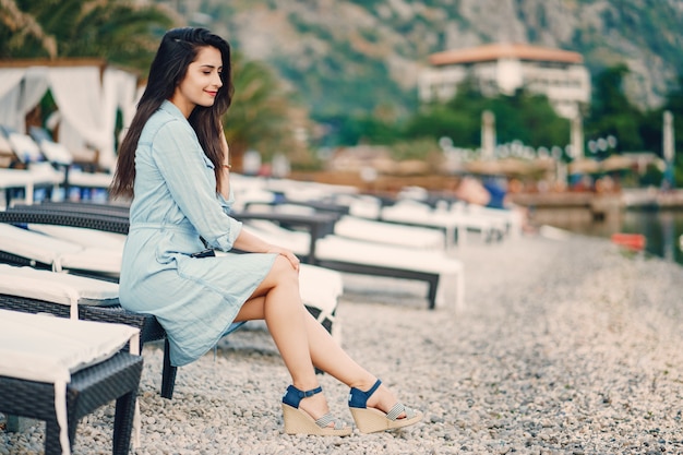 Uma linda garota jovem em um vestido azul, sentado perto da água e usar o telefone