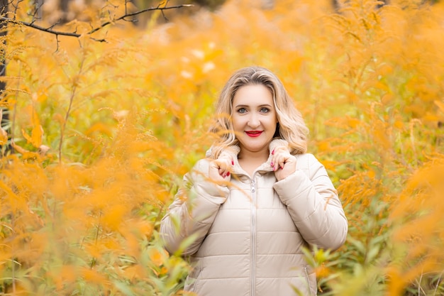 Uma linda garota loira está perto de um arbusto amarelo com uma jaqueta