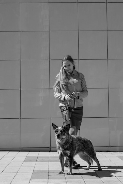 uma linda garota loira está segurando um cachorro curandeiro na coleira na cidade