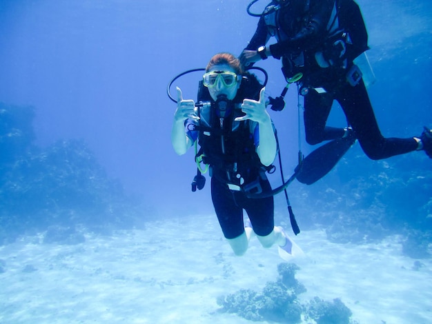Uma linda garota mergulhadora mostra sinal de gesto de mãos bem com um instrutor parceiro para segurança