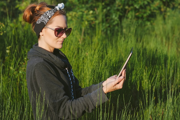 Uma linda garota na natureza tem um tablet nas mãos num contexto de uma bela vegetação.