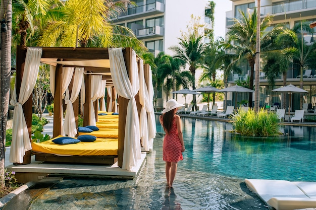 Uma linda garota posa no local perto da piscina, ao lado de camas e espreguiçadeiras ao ar livre. O conceito de turismo e lazer