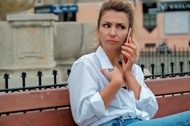 Uma linda garota se senta em um banco e segura um telefone nas mãos a garota pede comida pelo telefone a garota está falando ao telefone rindo feliz surpresa