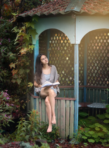 Uma linda garota se senta em um gazebo no verão com um livro