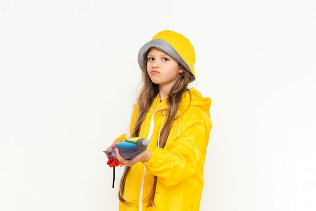 Uma linda garota segura um guarda-chuva fechado multicolorido em um fundo branco isolado Uma criança vestida com uma capa de chuva amarela e um chapéu panamá da chuva Conceito de tempo chuvoso