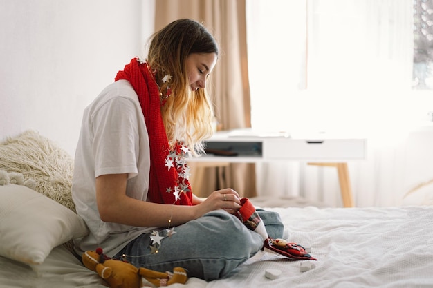 Uma linda garota segura uma meia de Natal nas mãos e tira algo dela Design de interiores confortável e aconchegante Trabalhe em casa Ano novo e conceito de Natal