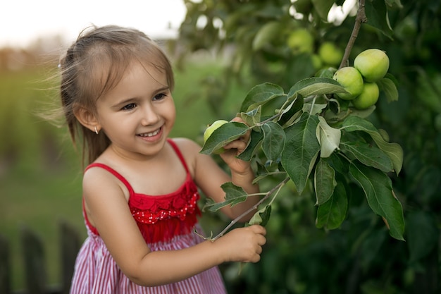 Uma linda garota sorridente ao lado de uma árvore com maçãs verdes verdes
